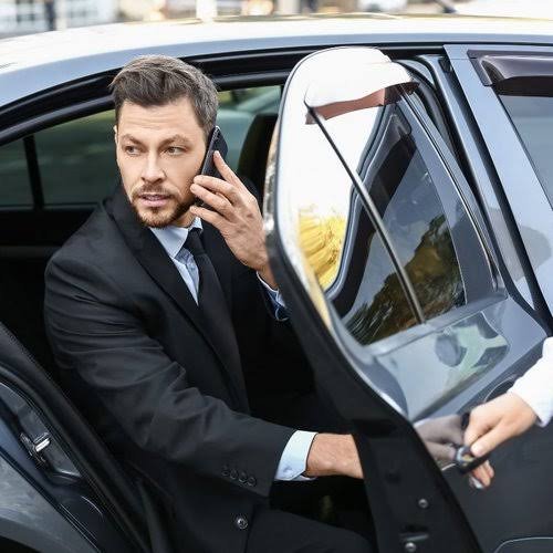 Hourly chauffeur service with businessman on phone exiting luxury vehicle