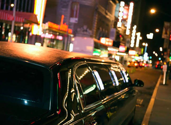 Night out limo service with black stretch limousine on a glowing city street at night